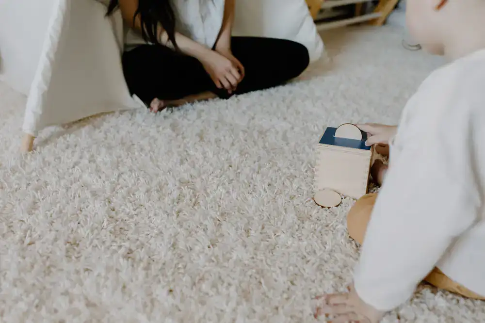 Child stacking wooden blocks on a rug in soft natural light