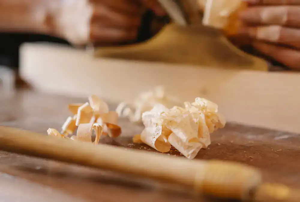 Close up of artisan sanding a wooden toy with wood shavings on the desk